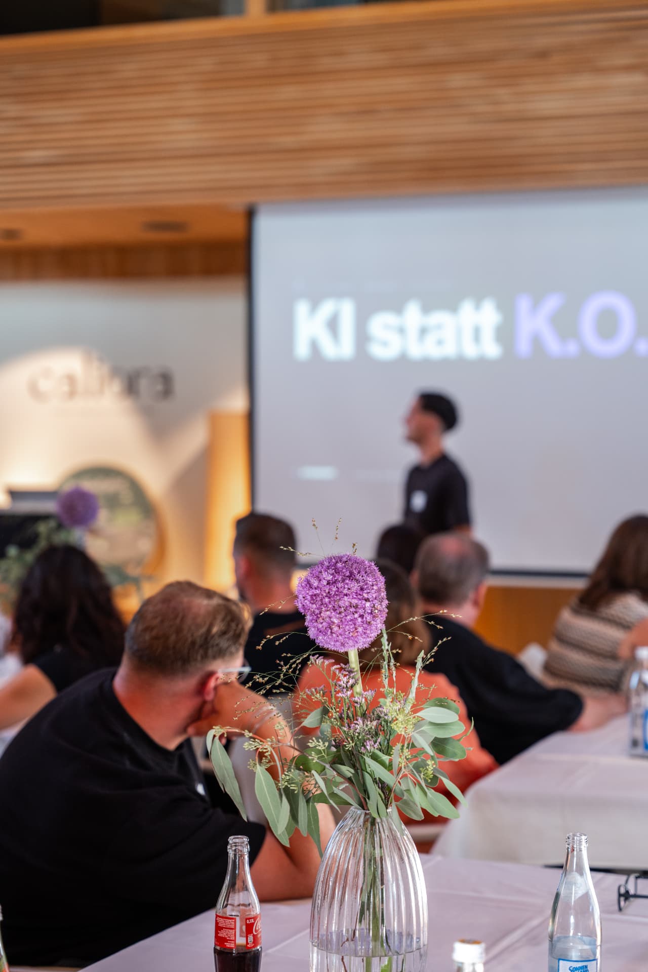 Blumendekoration im Vordergrund, Leinwand mit „KI statt K.O.“ im Hintergrund